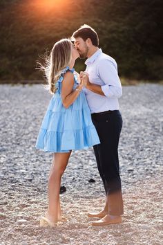 a man and woman kissing in front of the sun at their beach engagement photo shoot