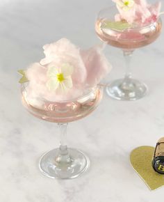 two wine glasses with flowers in them sitting on a table