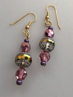 A lovely metallic drop earrings with loads of sparkle to dress up any holiday outfit. A fire polished central bead exhibits a purple tone which blends nicely with the faceted purple metallic beads on each side. The ear wire is nickel-free gold plate. Beaded Drop Earrings For Party, Party Beaded Drop Earrings With Ear Wire, Gold Crystal Earrings With Faceted Beads, Iridescent Beaded Drop Earrings, Elegant Faceted Beads Crystal Earrings For Party, Party Drop Earrings With Faceted Beads, Elegant Iridescent Beaded Earrings For Gift, Elegant Crystal Earrings With Faceted Beads For Party, Party Beaded Drop Earrings With Faceted Beads