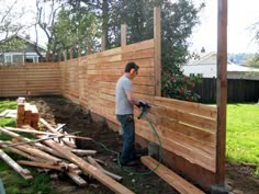 a man is using a power drill to build a fence in his backyard with wood