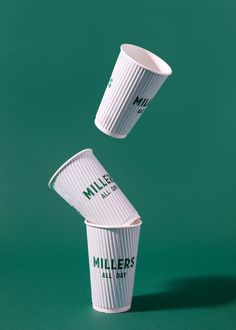 two white cups are flying in the air with their lids open on a green background