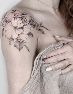 a woman with a flower tattoo on her shoulder and chest, holding onto the arm