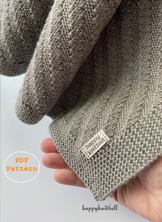 a hand holding a gray knitted sweater with a tag on it's side