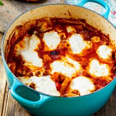 a blue pot filled with food sitting on top of a wooden table covered in sauce