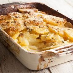 a casserole dish filled with potatoes on top of a wooden table and topped with parmesan cheese