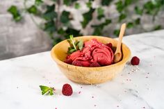 a wooden bowl filled with raspberries on top of a white marble countertop