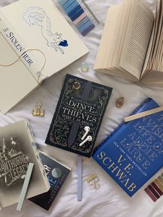 there are many books on the bed with white sheets and blue trimmings around them