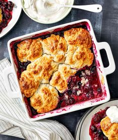 an image of berry cobbler with whipped cream on the top and two plates next to it