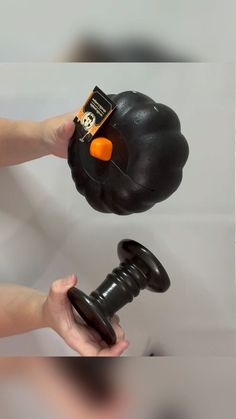 a person holding a black object with an orange button on it's side and another hand reaching for it