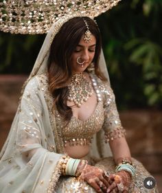 a woman in a bridal outfit sitting down with her hands on her chest and wearing jewelry