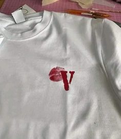 a white shirt with the letter v painted on it next to some scissors and tape