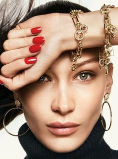 a woman with red nail polish holding her hands over her head and wearing gold bracelets