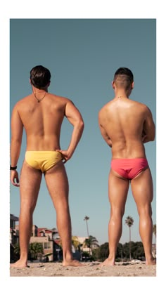 two men in swim trunks standing on the beach