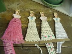 three paper dolls are sitting next to each other on a wooden table with doily