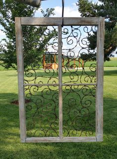 an old window with iron work on it in the middle of a grassy area next to trees