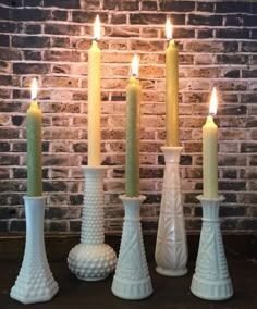 four white candles are lined up in front of a brick wall