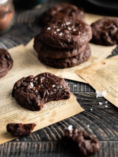 chocolate cookies with sea salt on top are sitting on parchment paper next to an old recipe book