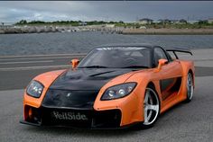 an orange and black sports car is parked by the water