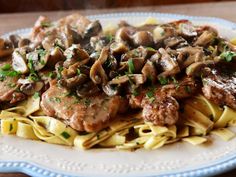 a white plate topped with pasta and meat covered in mushroom sauce on top of a wooden table