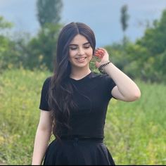 a woman in a black dress is smiling and posing for the camera with her hands behind her head