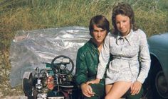 a man and woman sitting next to an old car