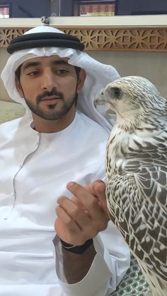 a man holding a falcon on his arm in front of the camera while wearing a white and black outfit