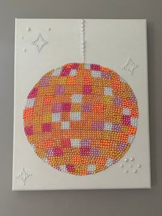 an orange and pink beaded ornament hanging on a white canvas with stars