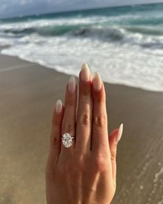 a woman's hand holding a diamond ring on the beach with waves in the background