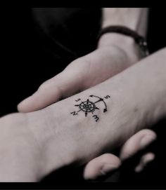 two hands holding each other with small tattoos on their wrists and fingers, one has a compass tattoo on it's left wrist