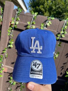 a baseball cap with the dodgers 47 clean up on it is held in front of a fence