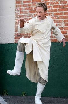 a man dressed in white is standing on the street with his arms out and one foot up