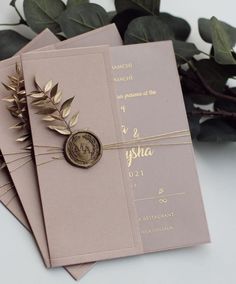 the wedding stationery is adorned with a wax stamp and gold leafy accents, along with some greenery