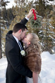 a bride and groom kissing in the snow with a christmas wreath on their foreheads