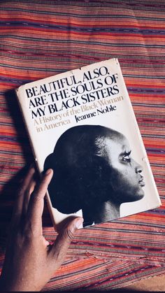 a person holding up a book on top of a striped cloth covered tablecloth with the title beautiful aso are the souls of my black sisters