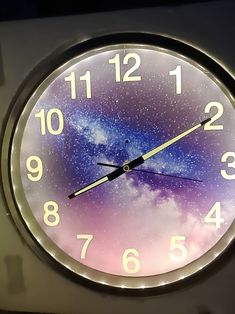 a clock with the sky and stars painted on it's face is lit up