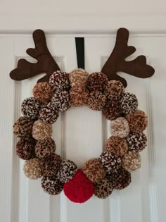 a christmas wreath with reindeer antlers hanging on the front door, decorated with brown and red pom - poms