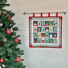 a christmas quilt hanging on the wall next to a tree with red balls and ornaments