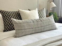 a bed topped with lots of pillows next to a night stand and window sill