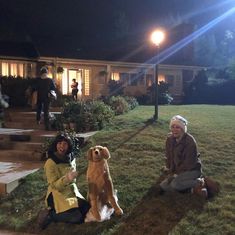 two women and a dog sitting on the grass in front of a house at night