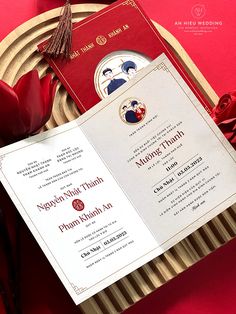 a red and white wedding card on top of a wooden plate with flowers in the background