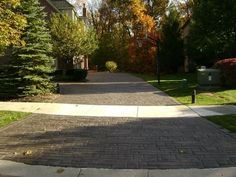 a brick sidewalk in front of a house with trees lining the street and bushes on both sides