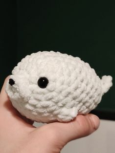 a hand holding a small white crocheted object with black eyes on it's face