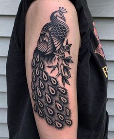 a black and white tattoo of a peacock on the left arm with leaves around it