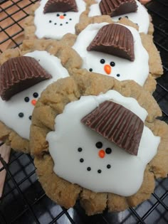 cookies decorated like snowmen with chocolate hats on top are cooling on a grill rack