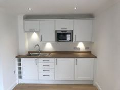 an empty kitchen with white cabinets and wood flooring in the middle of the room