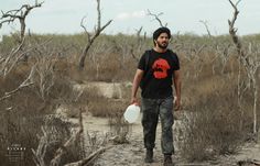 a man holding a white frisbee walking through a dry grass covered forest filled with dead trees