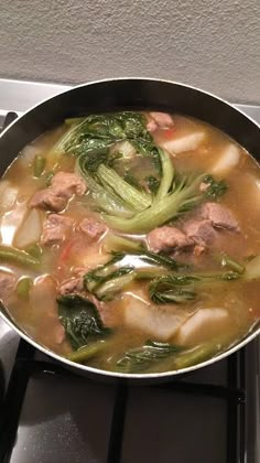 a pan filled with meat and veggies on top of a stove burner