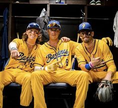 three baseball players sitting in the dugout posing for a photo with their hats on