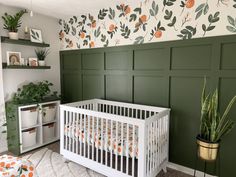 a white crib in front of a green wall with oranges and leaves on it