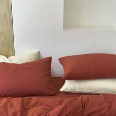 a bed with red sheets and pillows on top of it, in front of a white wall